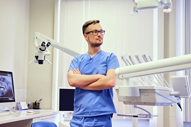 Male dentist in a room with medical equipment on background.